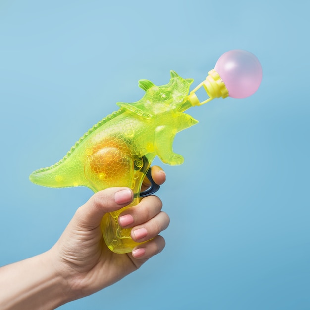 Free photo hand holding a water gun in the form of a rhinoceros blowing a bubble