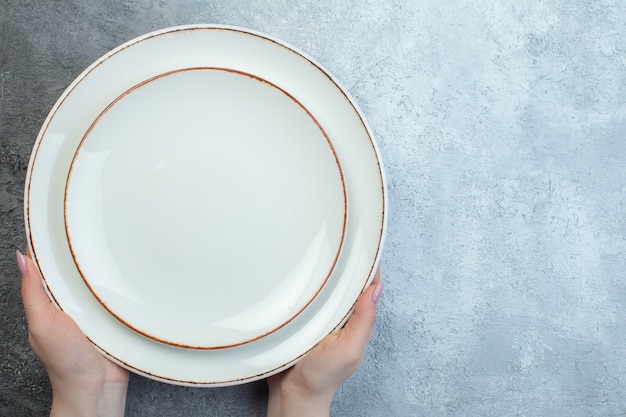Hand holding white plates on the right side on half dark light gray surface with distressed coarse-grained gradient surface