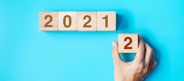 Рука деревянный кубик с текстом 2022 года на синем фоне. решение, план, обзор, цель, начало и концепции новогодних праздников