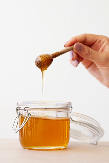 Hand holding wooden honey dipper from honey jar