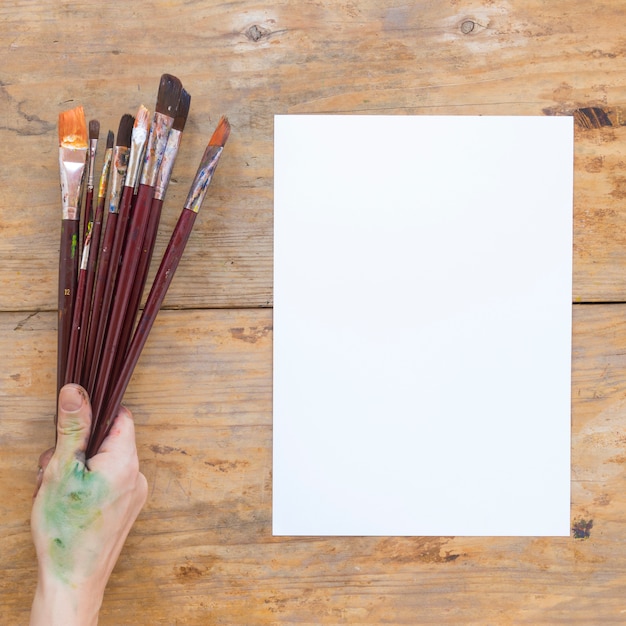 Hand holding wooden paint brushes near white paper