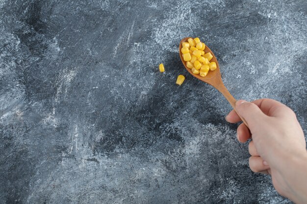 Hand holding a wooden spoon full of popcorn seeds .