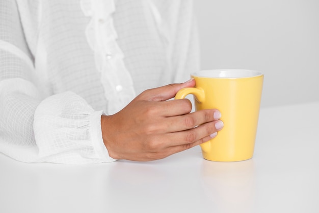 Hand holding yellow cup on a table