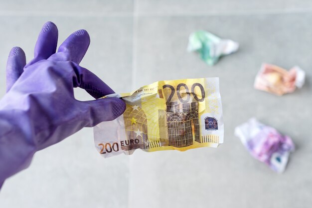 회색에 구겨진 유로 지폐를 들고 청소용 보라색 고무 장갑에 손을 프리미엄 사진
