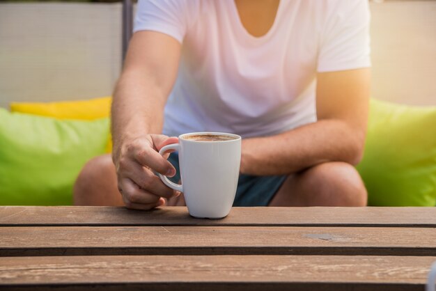 Hand is holding a coffee cup.Men are drinking morning coffee  with a green background outside. Man hands holding cup of coffee at cafe outdoors summer