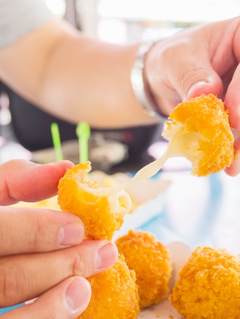 La mano è in possesso di una palla di formaggio stretch pronta per essere mangiata con patatine fritte morbide e concentrate