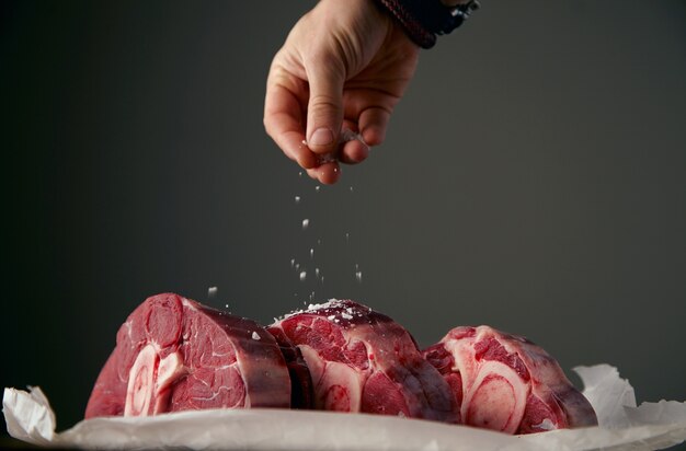 手は骨付きの3つの新鮮な肉ステーキをサットリングしています