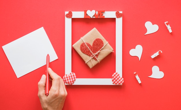 Free photo hand near paper, frame with love title, present and heart symbols