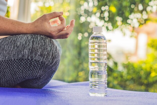 ヨガ​の​敷物​と​水​の​ボトル​で​ヨガ​の​ポーズ​で​瞑想している​女性​の​手