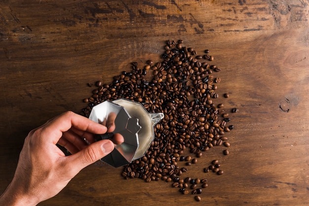 Free photo hand opening cap of coffee maker near coffee beans