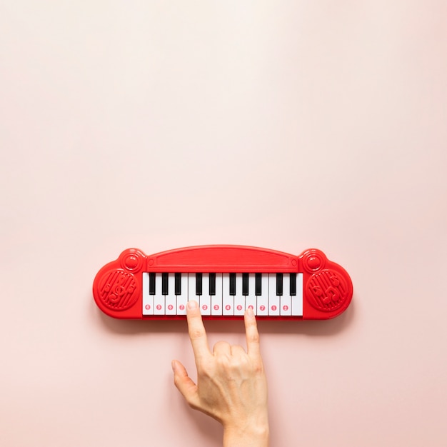 Free photo hand and piano toy on pink background