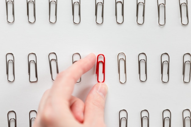 Hand picking among metal paperclips one red, different from others