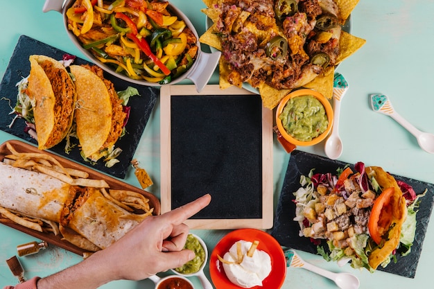 Hand pointing at blackboard amidst Mexican dishes