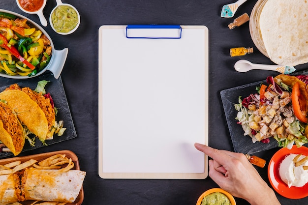 Hand pointing at clipboard among mexican food