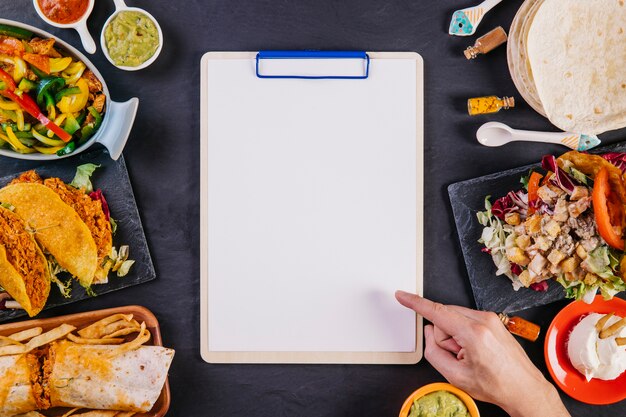 Hand pointing at clipboard among Mexican food