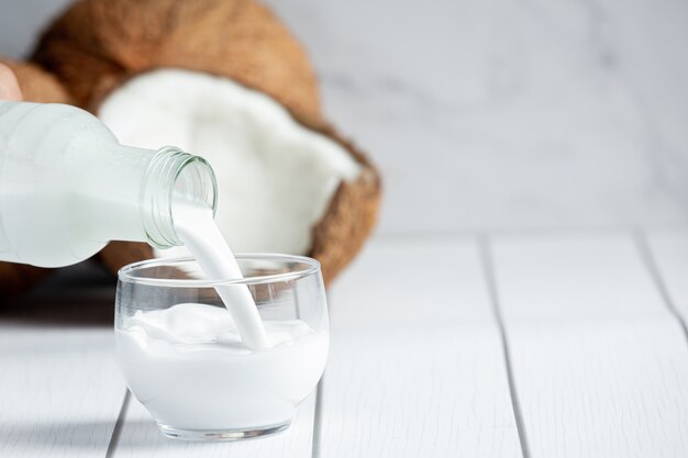 Рука наливает кокосовое молоко из бутылки в стакан