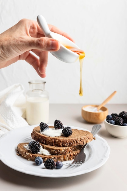 Foto gratuita mano che versa miele su pane tostato con mirtilli