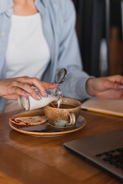 一杯のコーヒーに牛乳を注ぐ手