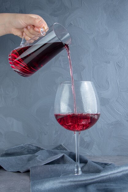 Hand pouring pomegranate juice in a glass cup with ice cubes