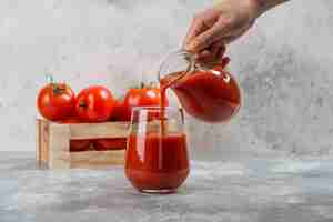 Foto gratuita mano che versa il succo di pomodoro in una tazza di vetro.