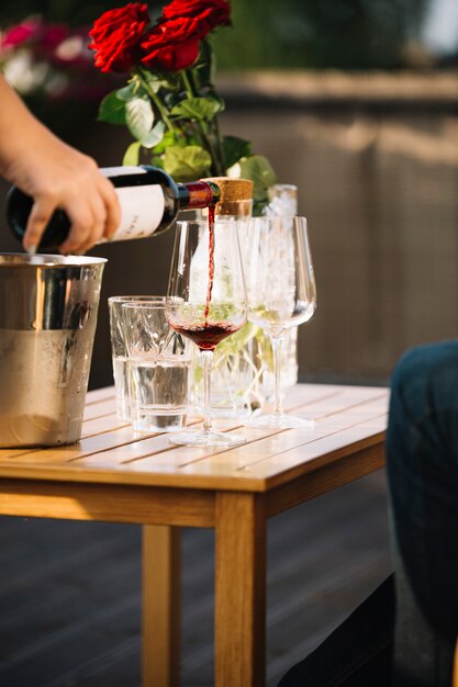 Hand pouring wine in transparent glass on wooden table
