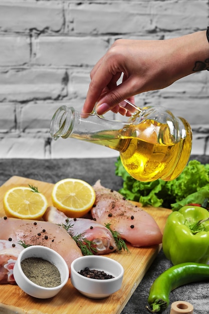 Hand pours oil to plate of raw chicken meats with bunch of vegetables.