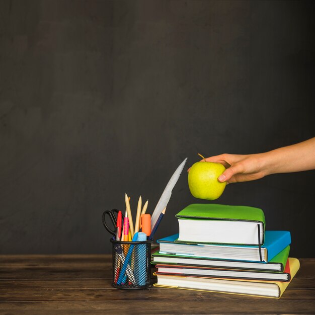 hand putting apple on textbooks on workplace