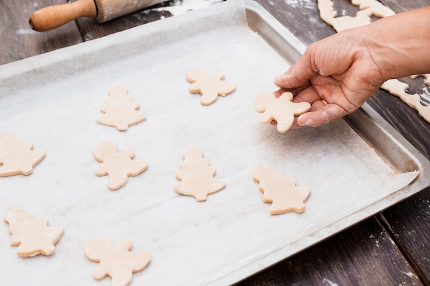 Free photo hand putting christmas shaped cookies on baking sheet