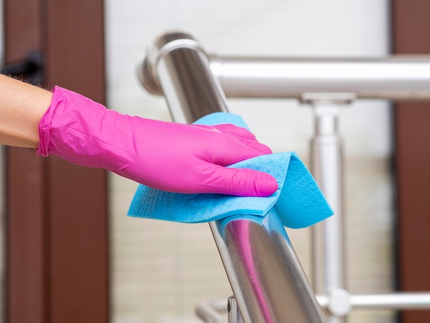 Hand rail being disinfected by person with cloth and surgical glove