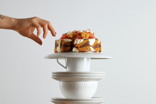 A hand reaching out to grab a piece of beautiful light brown sponge cake with chocolate and cream and grapefruit