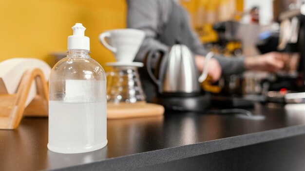 Hand sanitizer of the coffee shop counter with defocused male barista