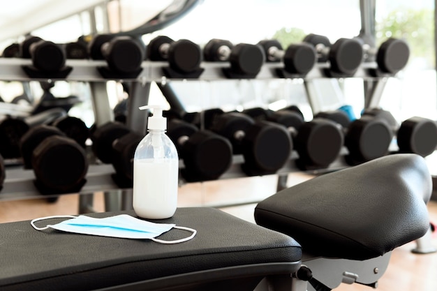 Hand sanitizer and medical mask on gym bench