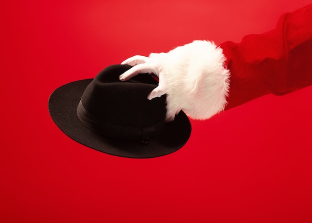 赤の背景に黒い帽子を保持しているサンタクロースの手。季節、冬、休日、お祝い、ギフトのコンセプト