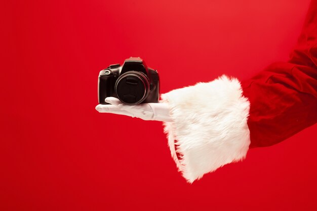 빨간색 배경에 카메라를 들고 산타 클로스의 손. 계절, 겨울, 휴일, 축하, 선물 개념