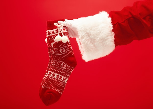 Рука Санта-Клауса, держащая рождественские вязаные носки на красном