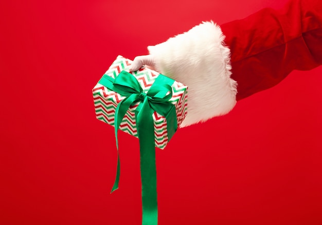 The hand of santa claus holding a gift on red background. The season, winter, holiday, celebration, gift concept