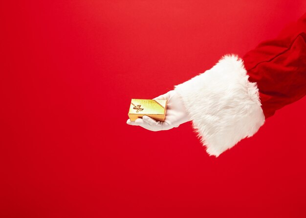 빨간색 배경에 선물을 들고 산타 클로스의 손. 계절, 겨울, 휴일, 축하, 선물 개념