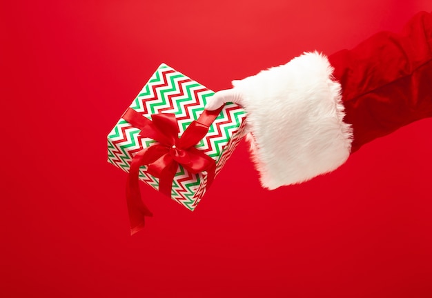 The hand of santa claus holding a gift on red