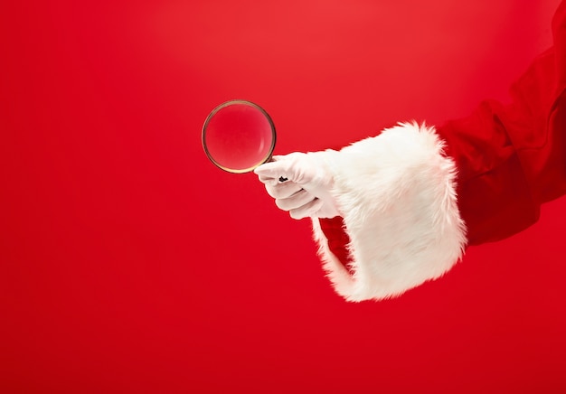 Free photo the hand of santa claus holding a magnifier on red