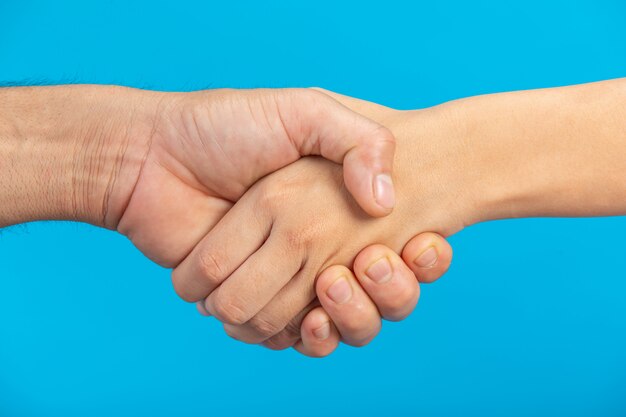 Hand shake between young boy and young girl on blue wall.