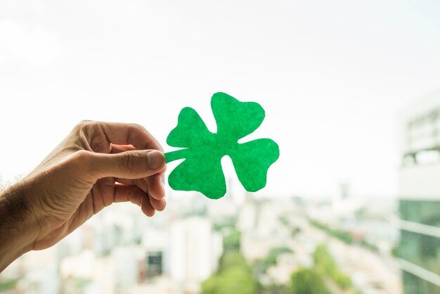 Hand showing green paper shamrock and view of cityscape