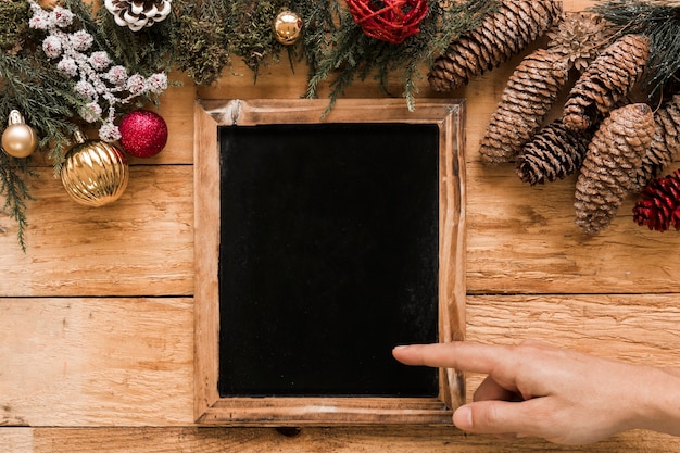 Free photo hand showing on photo frame near coniferous twigs, snags and christmas balls