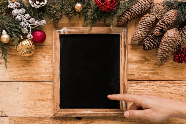 Hand showing on photo frame near coniferous twigs, snags and Christmas balls