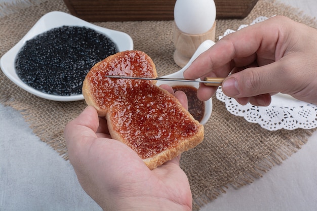 Hand slathers jam on bread with knife.