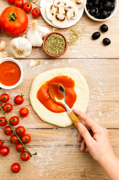 Hand spreading tomato sauce on pizza dough