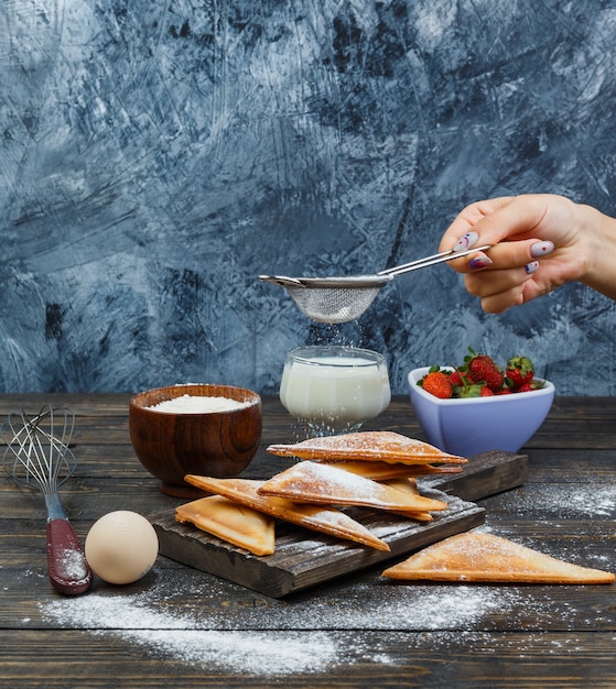 Hand sprinkling flour on waffle on wooden board