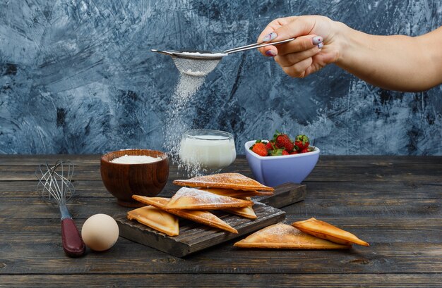 Hand sprinkling flour on waffle on wooden board