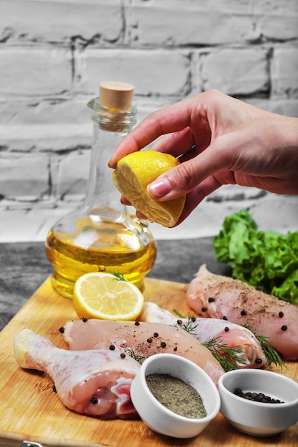Выдавите рукой свежий лимон на тарелку сырого куриного мяса с кучей овощей.