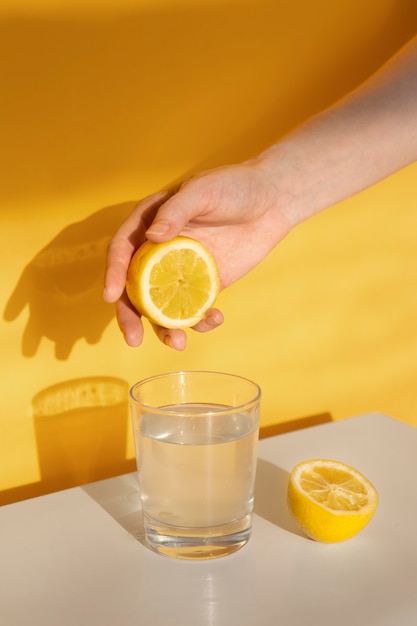 Рука выжимает лимон в стакан с водой под высоким углом