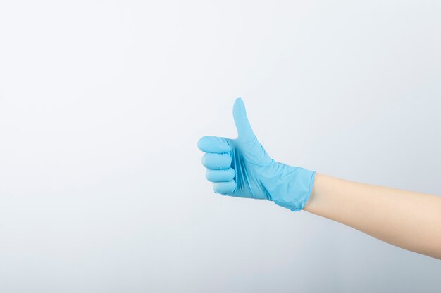 Hand of surgeon in blue medical glove showing a thumb up. 
